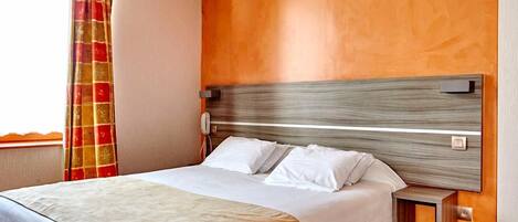 Une chambre d’hôtel avec un grand lit, une tête de lit en bois, une table de chevet et une fenêtre avec des rideaux.