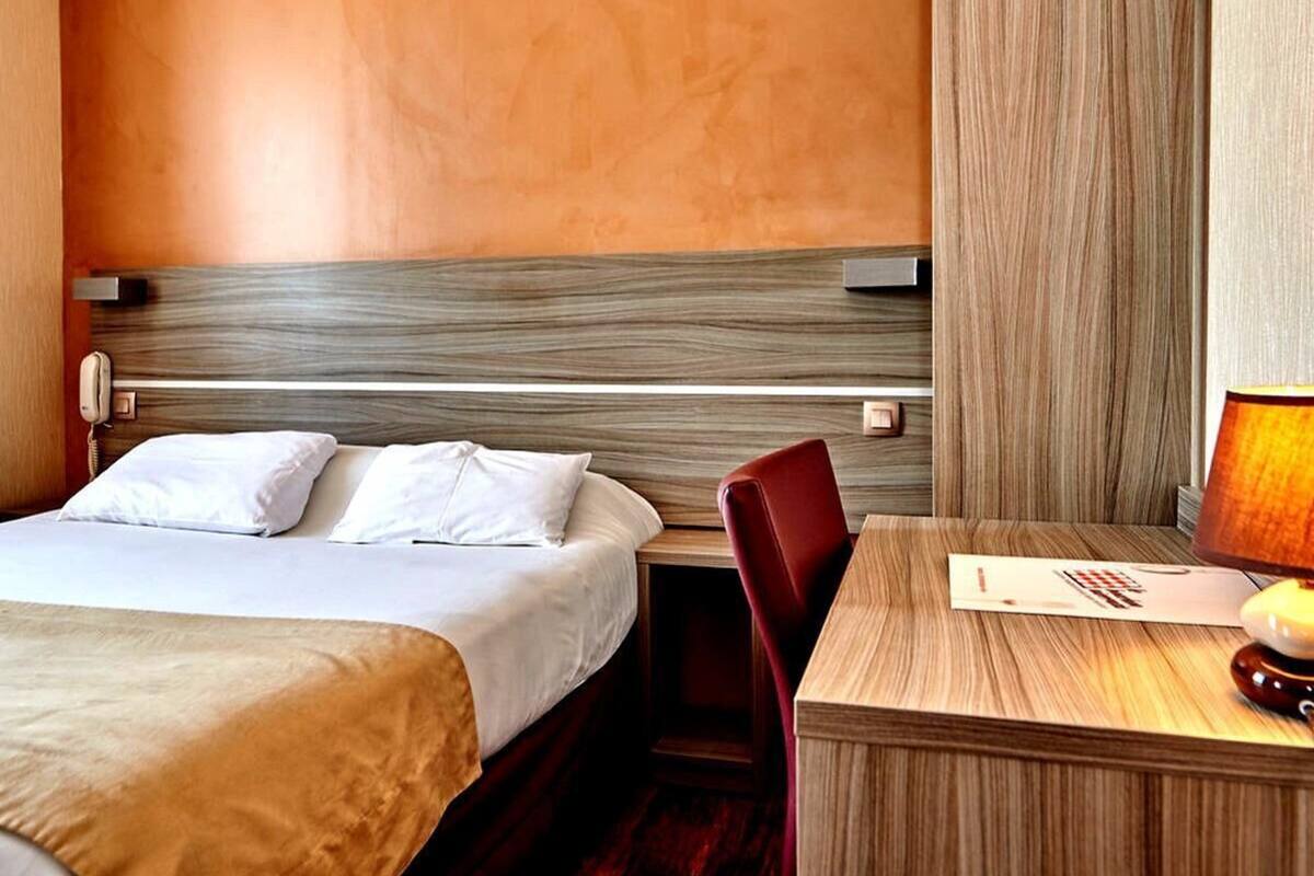 A hotel room with a bed, a desk, a chair, and a lamp.