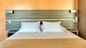 Una cama bien hecha con cabecera de madera, dos almohadas y una mesita de noche con un teléfono.