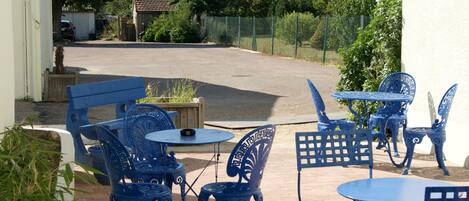 Un patio al aire libre con sillas y mesas de metal azul, rodeado de follaje y una valla.