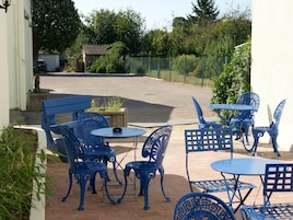 Un patio al aire libre con sillas y mesas de metal azul, rodeado de follaje y una valla.