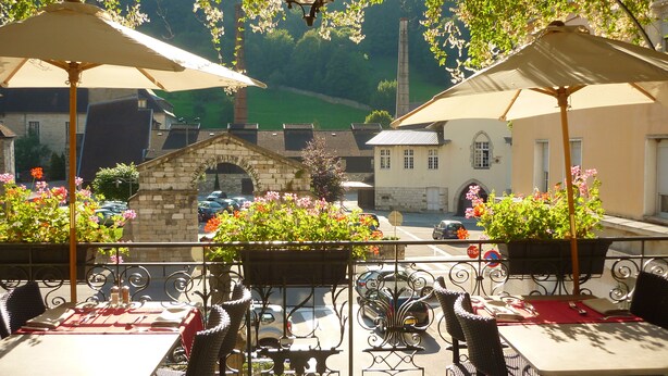 An outdoor café with tables and chairs, surrounded by stone walls and greenery.