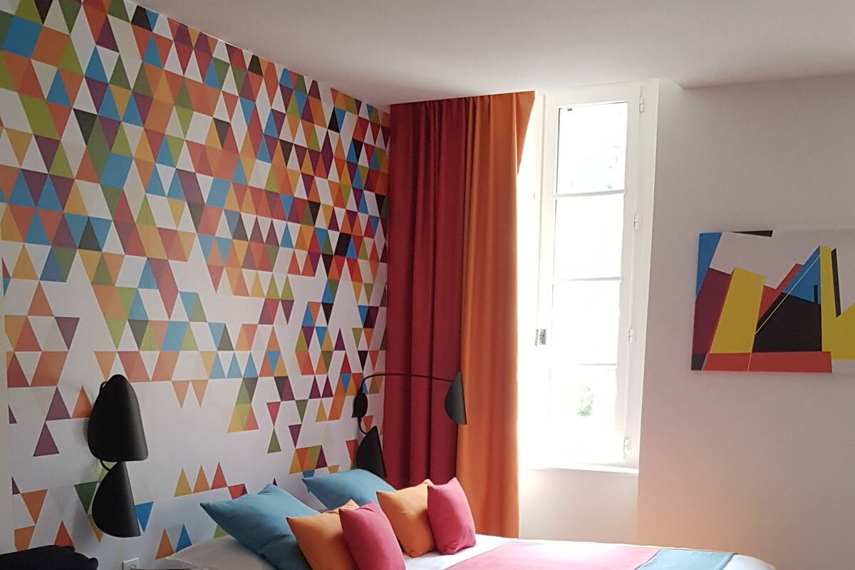 A bedroom with a bed, a sofa, a geometric-patterned wall, and a window with curtains.