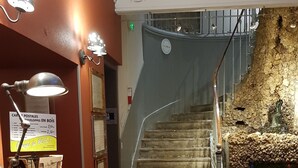 A reception desk with a telephone, a signboard, and a flower vase. A staircase with a stone wall is visible in the background.