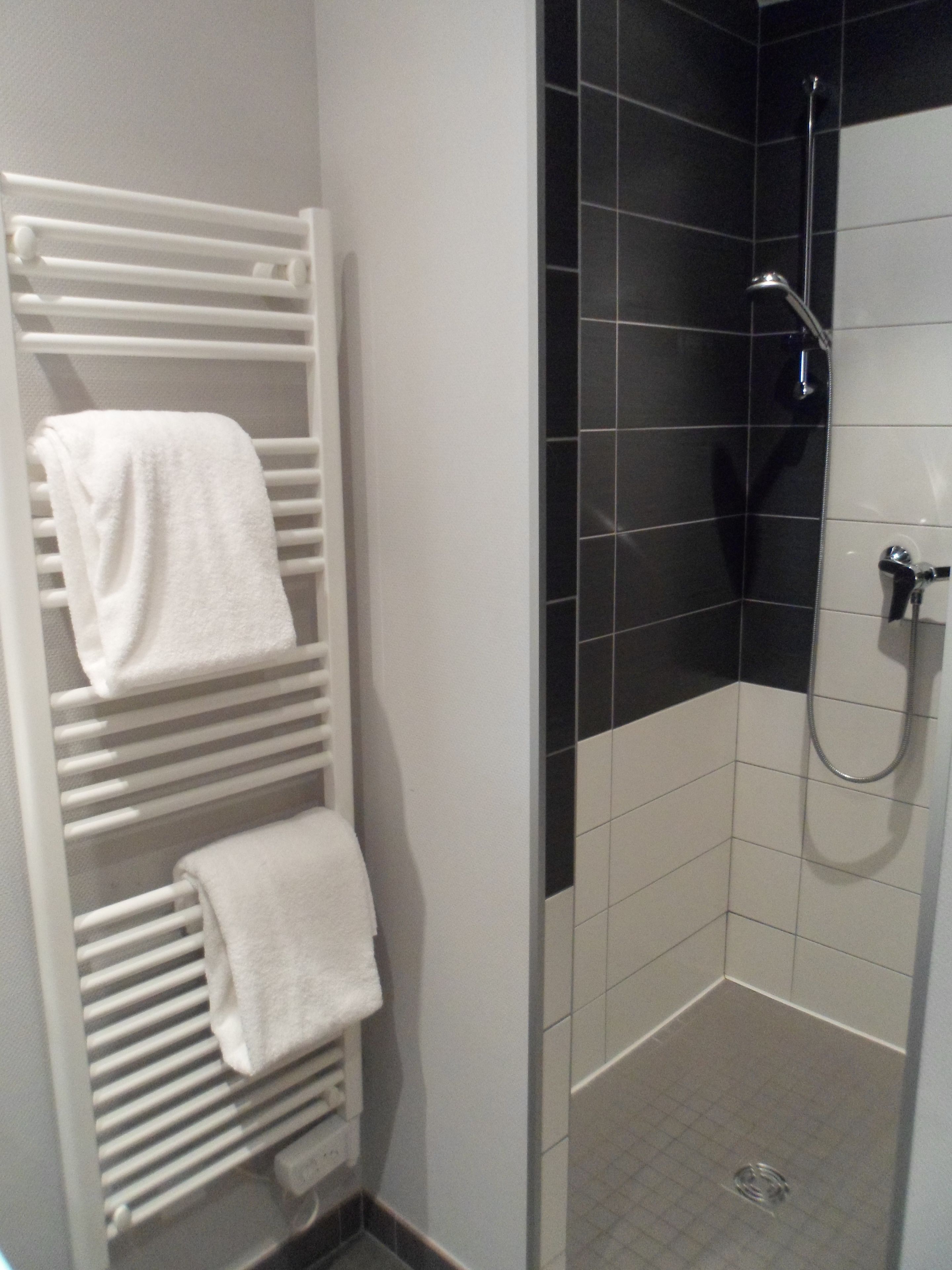 A bathroom with a white towel rack, a shower with black tiles, and a white tiled floor.
