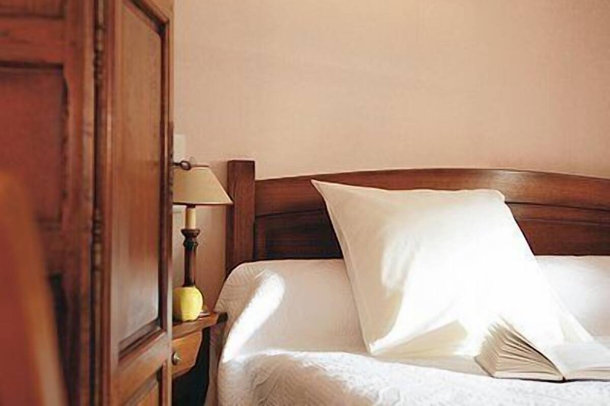A neatly made bed with a wooden headboard, a bedside lamp, and an open book on the bed.