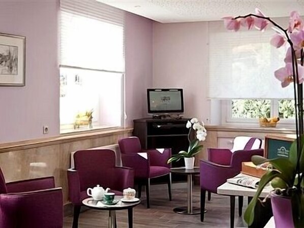 A room with purple chairs, a small table with a teapot and cups, a television, and a window with blinds. - Hôtel CARRER Le Rhien (Ronchamp)