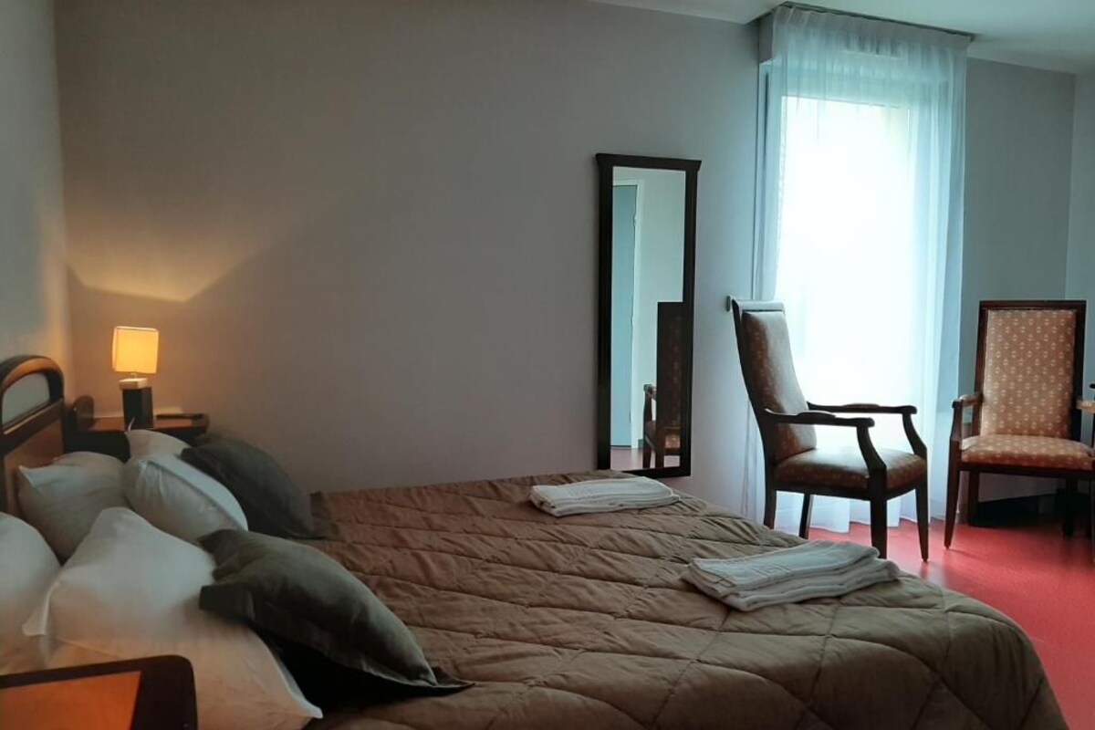 A hotel room with a bed, two chairs, a nightstand with a lamp, and a mirror.
