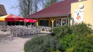 An outdoor seating area with tables and chairs, a covered patio, and a building with a red roof. - Hôtel le Grand Terre (Chartronges)