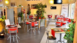 A restaurant with red and grey chairs, tables, and a large plant in the center. - Hôtel le Grand Terre (Chartronges)