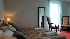 A hotel room with a large bed, two chairs, a desk with a lamp, and a mirror. - Hôtel le Grand Terre (Chartronges)