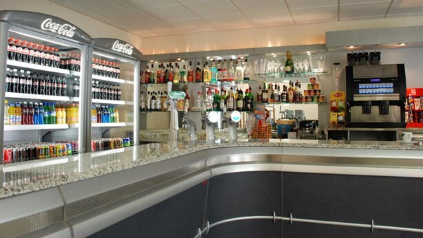 A bar area with shelves stocked with various beverages, including Coca-Cola, and a coffee machine. - Hôtel le Grand Terre (Chartronges)