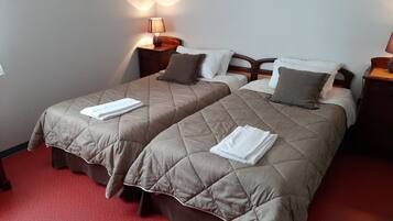 A hotel room with two beds, each with a quilted bedspread and pillows, a nightstand with a lamp, and a red carpeted floor.