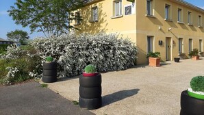 A yellow building with a sign for 'Hotel St. Bénigne'. There are potted plants and a bush with white flowers in front. - Hôtel le Grand Terre (Chartronges)