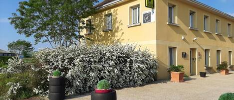 Un edificio amarillo con un letrero que dice 'Hotel St. Bénigne'. Hay plantas en macetas y un arbusto con flores blancas en la fachada.