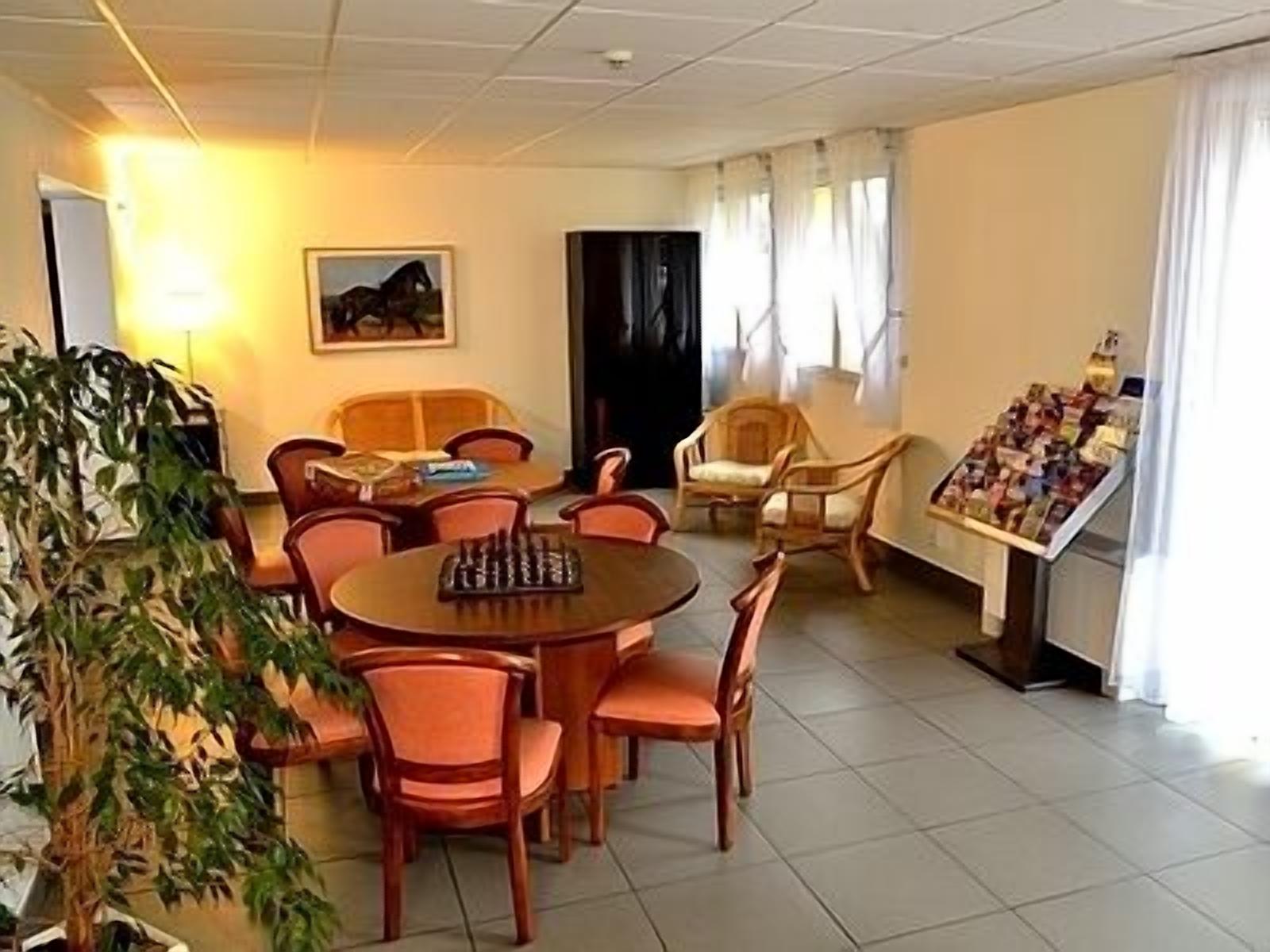 Habitación de hotel con comedor, un gran ventanal con cortinas, una planta y un tablón de anuncios con varios objetos.