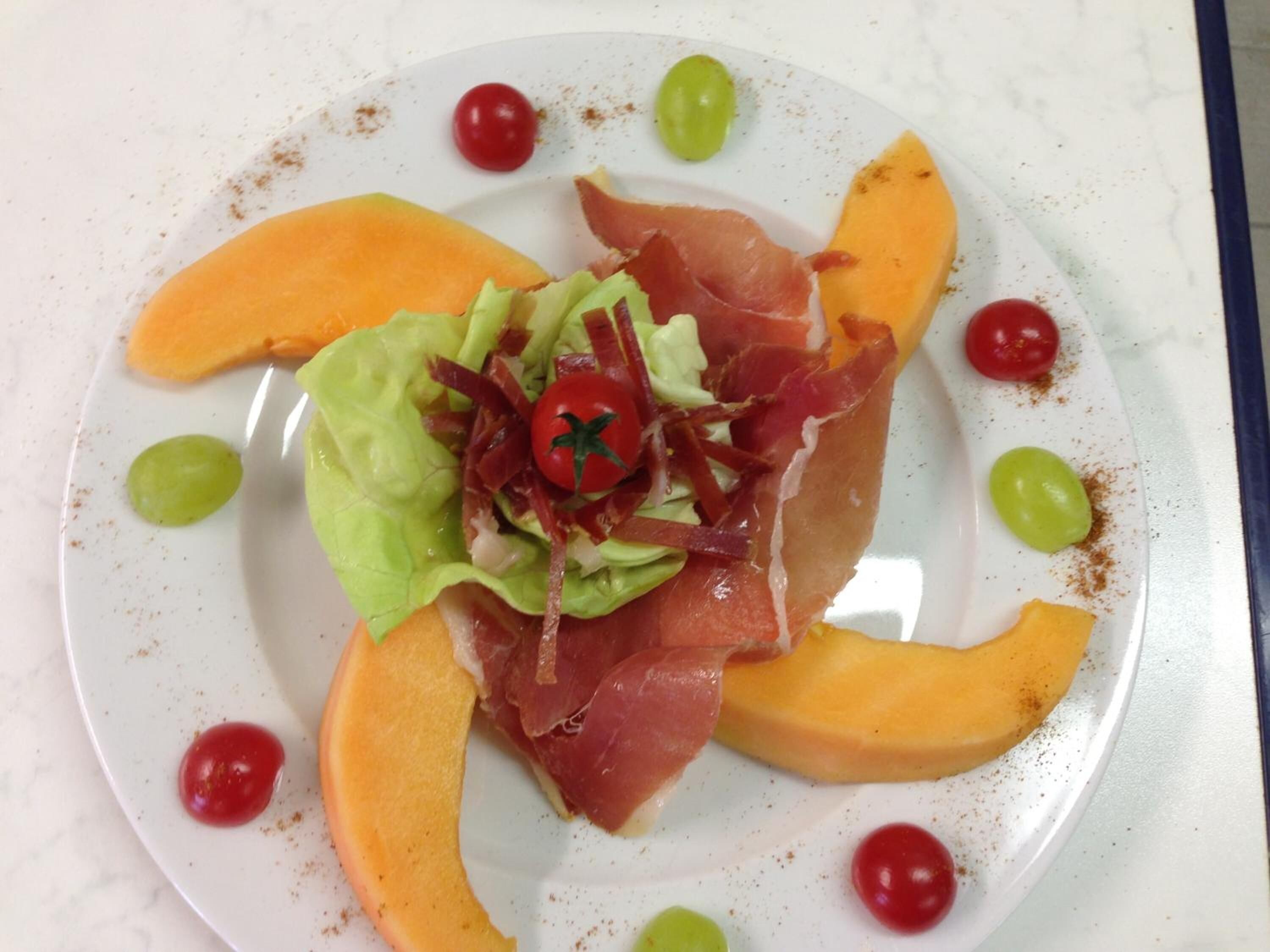 A plate with a salad of lettuce, cherry tomatoes, and prosciutto, surrounded by slices of mango.