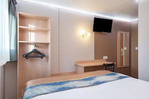 A hotel room with a bed, a desk, a chair, a TV, and a wardrobe.