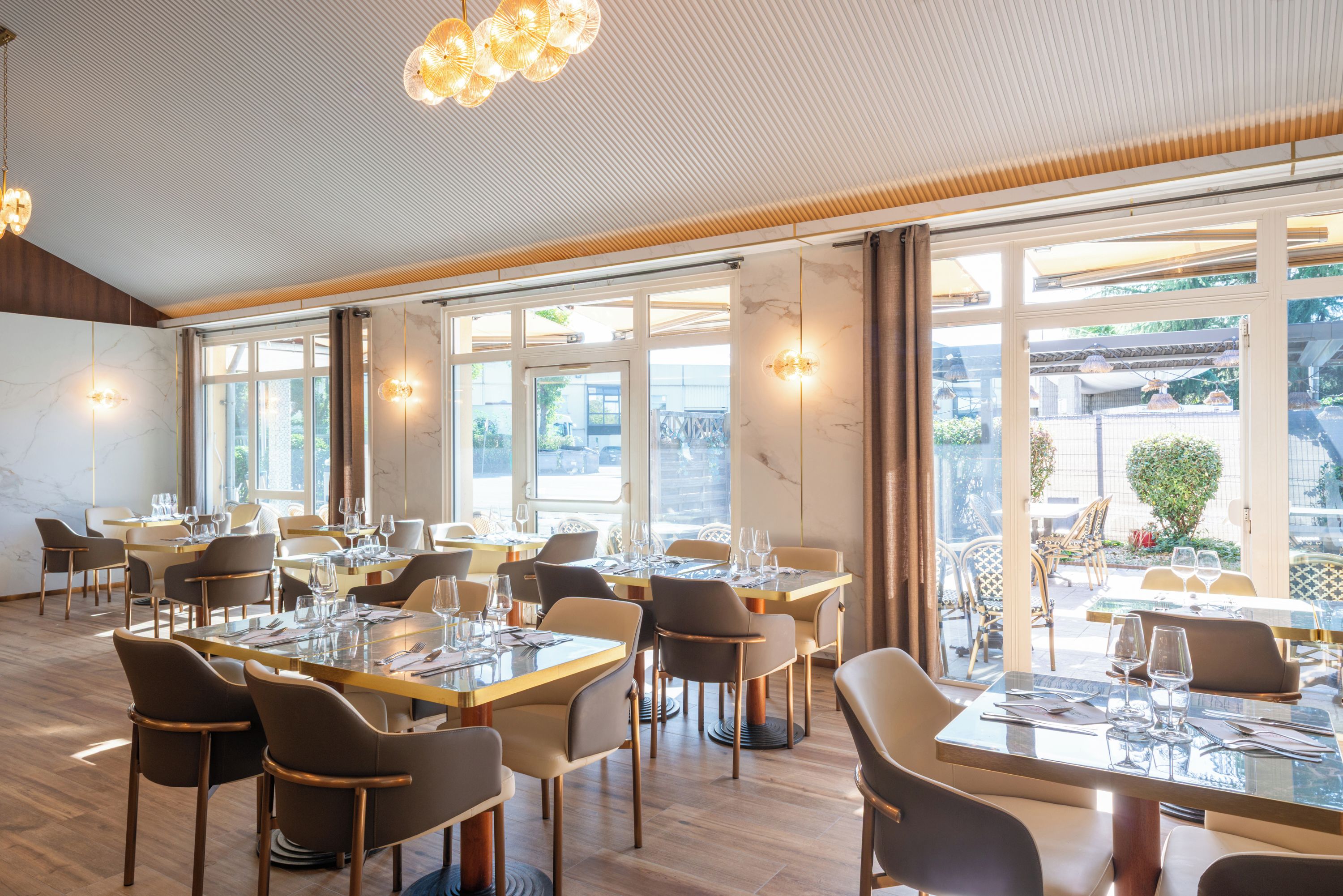 Un restaurant doté de nombreuses tables et chaises, de grandes fenêtres et d’un plafond orné d’un luminaire original.