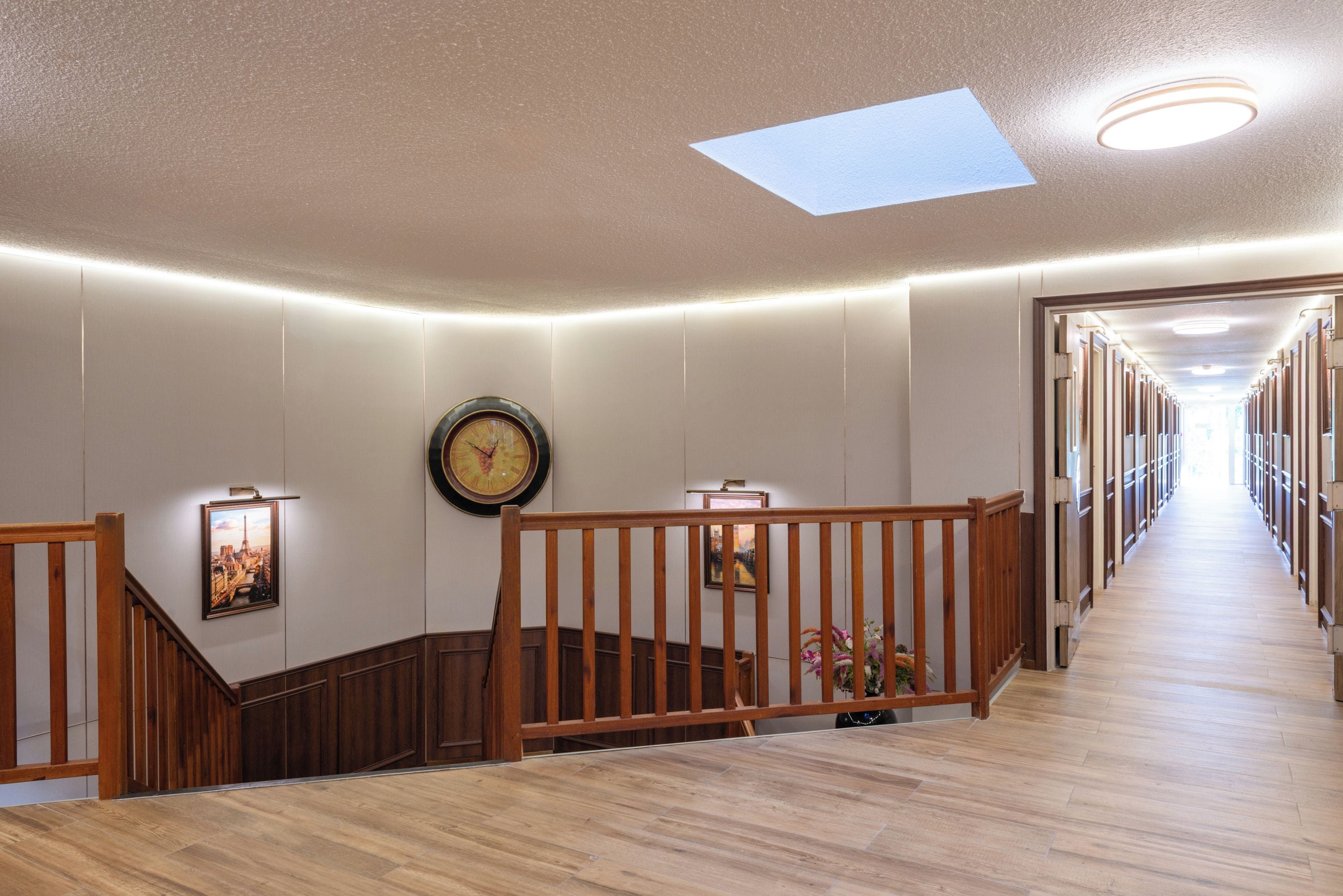 A hotel hallway with a wooden staircase, a clock, and a skylight.