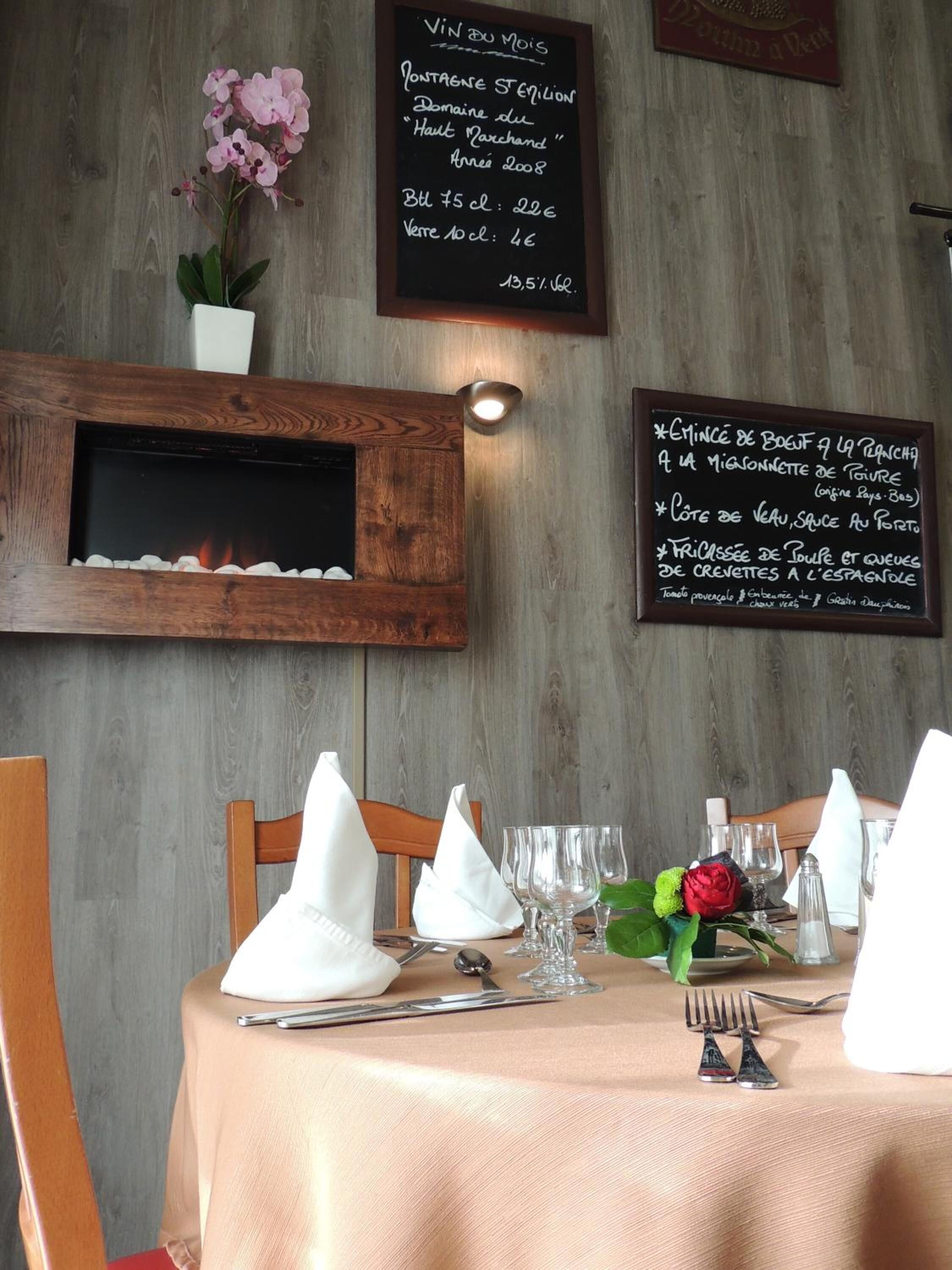 A restaurant interior with a wooden wall, a chalkboard menu, and a table set for dining.