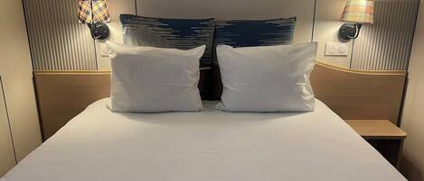 A hotel room with a large bed, two pillows, a nightstand, and two wall-mounted lamps.