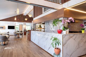Un moderno vestíbulo de hotel con una recepción de mármol, suelo de madera y una zona de comedor con mesas y sillas.