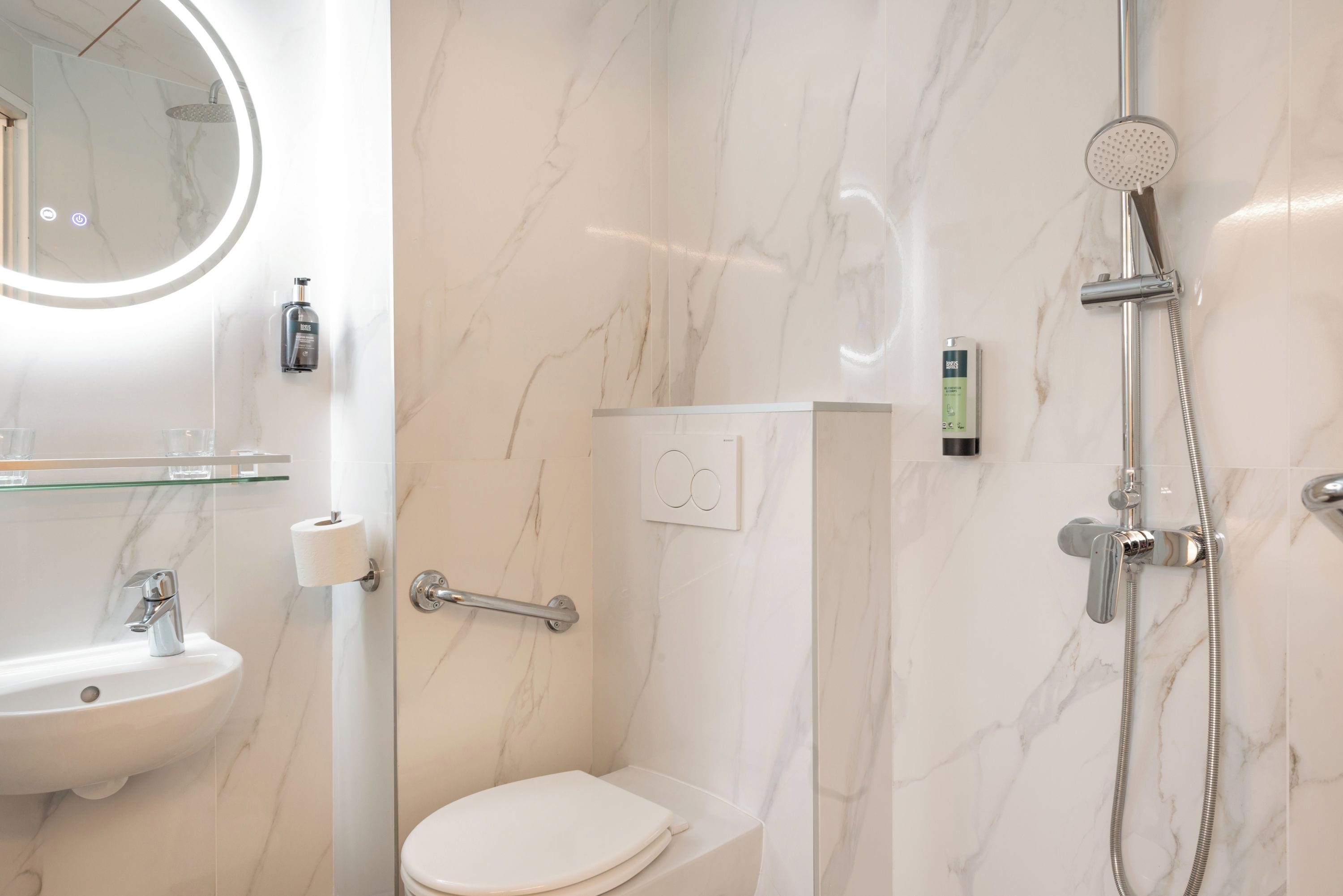 Un baño moderno con piso de mármol, un espejo redondo, un inodoro, un lavamanos y una ducha.