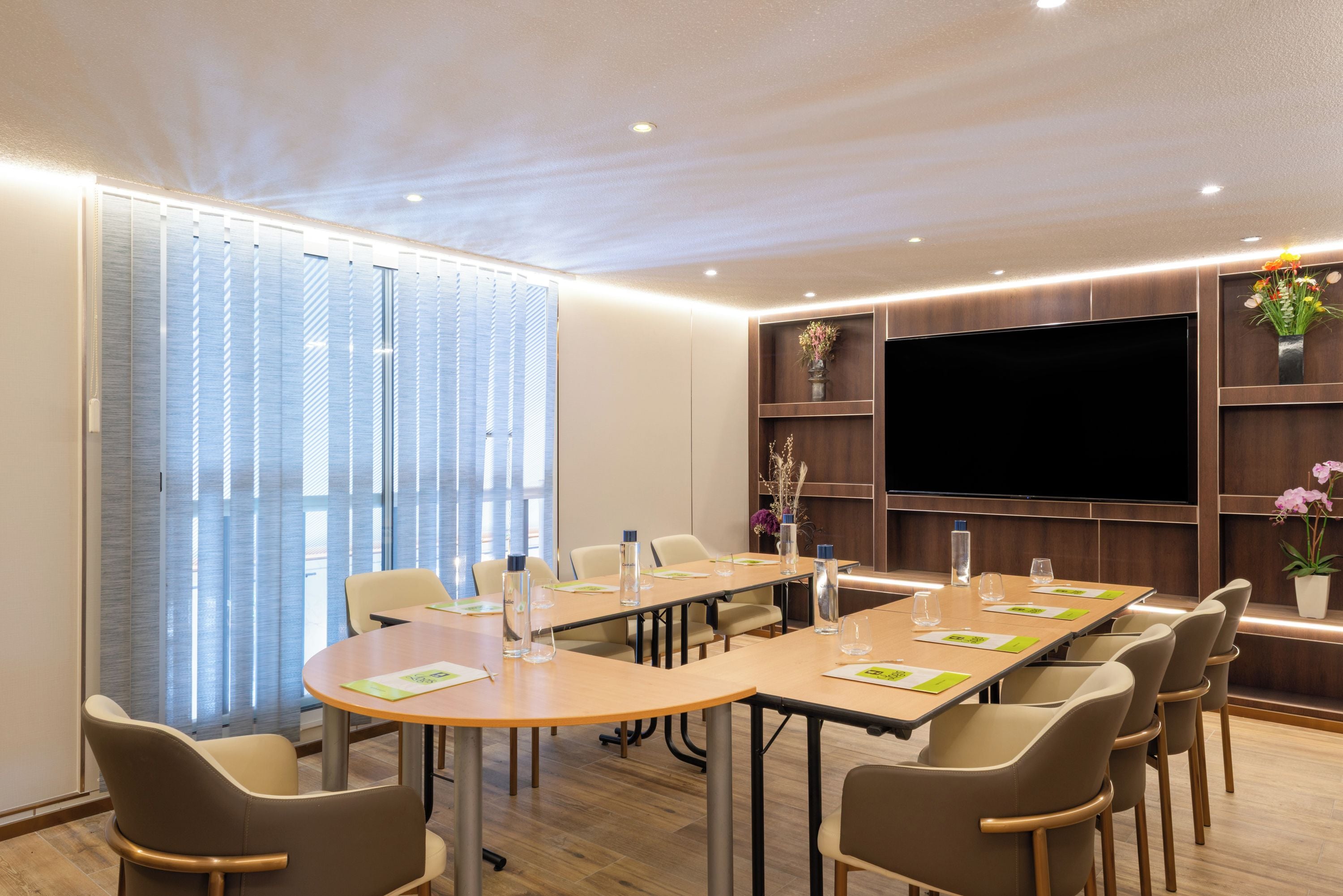 A conference room with a long table, chairs, a flat-screen TV, and wooden shelving with decorative items.