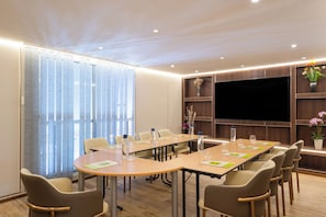 A conference room with a long table, chairs, a flat-screen TV, and wooden shelving with decorative items.