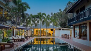 A poolside area with lounge chairs, a dining area, and a building with large windows.