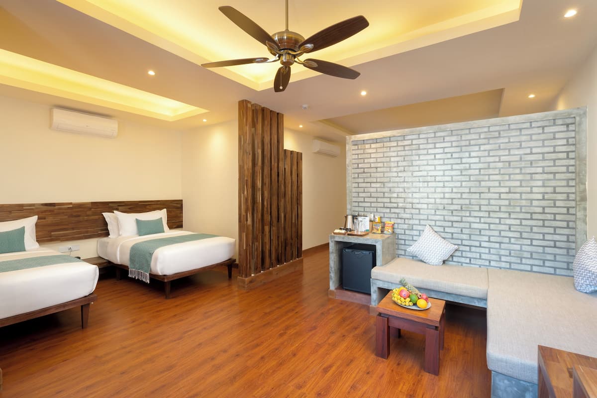 Une chambre d’hôtel avec deux lits, un ventilateur de plafond, un mur en briques, un canapé et une petite table sur laquelle se trouve des fruits.