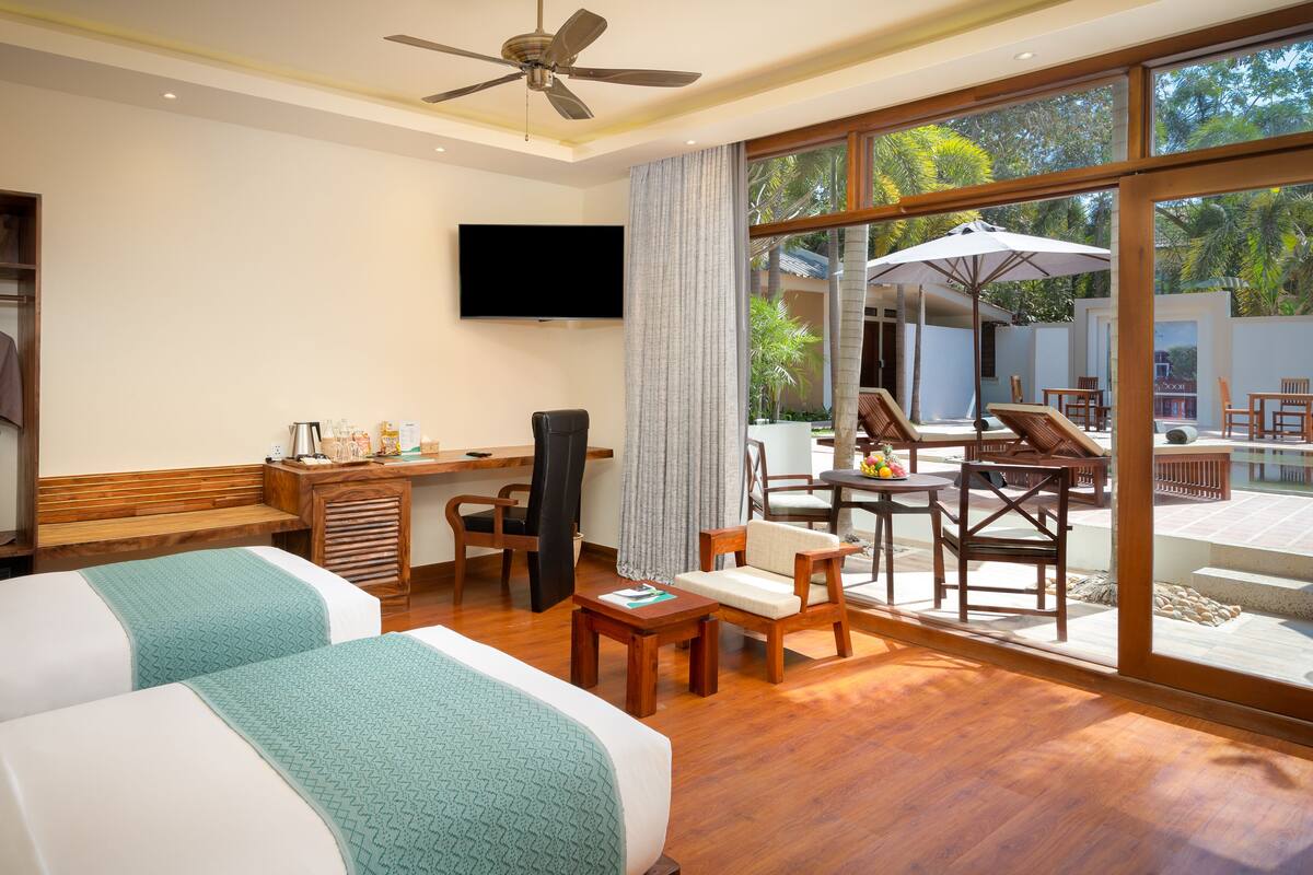 Une chambre d’hôtel avec deux lits, un bureau avec une chaise, une télévision et un balcon avec des meubles d’extérieur.