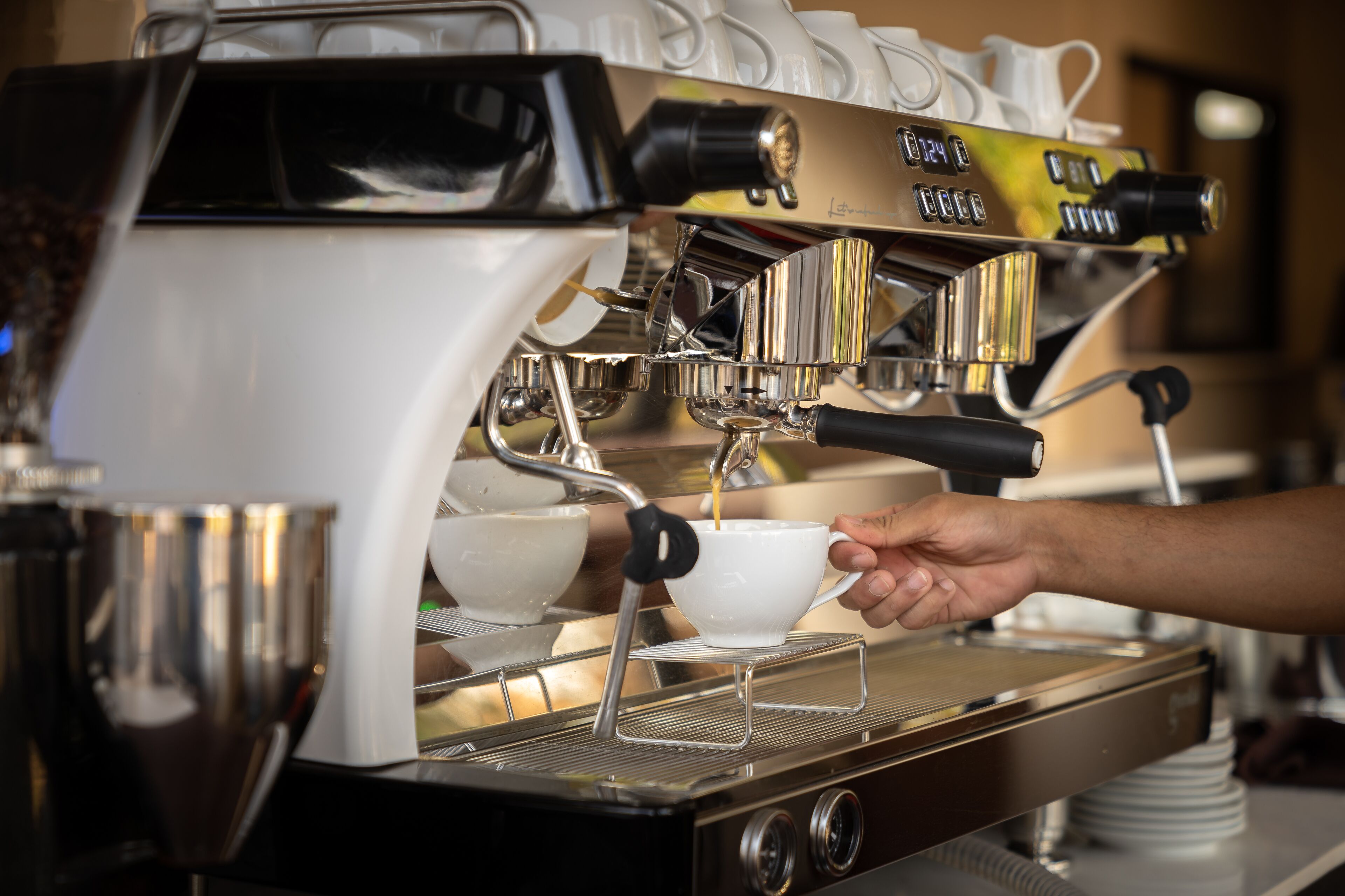 Close-up van een koffieapparaat, een hand houdt een kopje onder de tuit.
