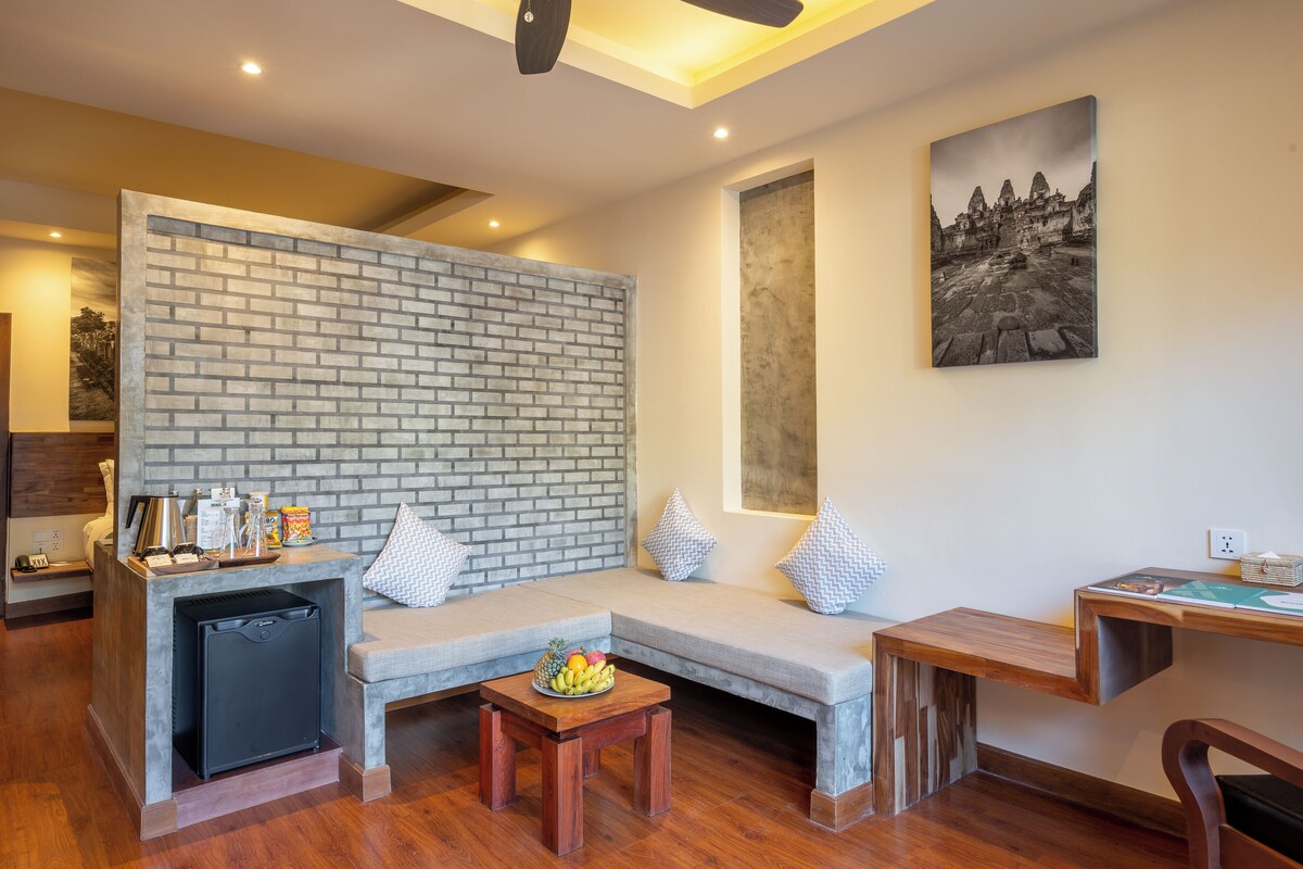 Una sala moderna con pared de ladrillo decorativa, una zona de estar con cojines, una mesita con fruta y una obra de arte colgada en la pared.