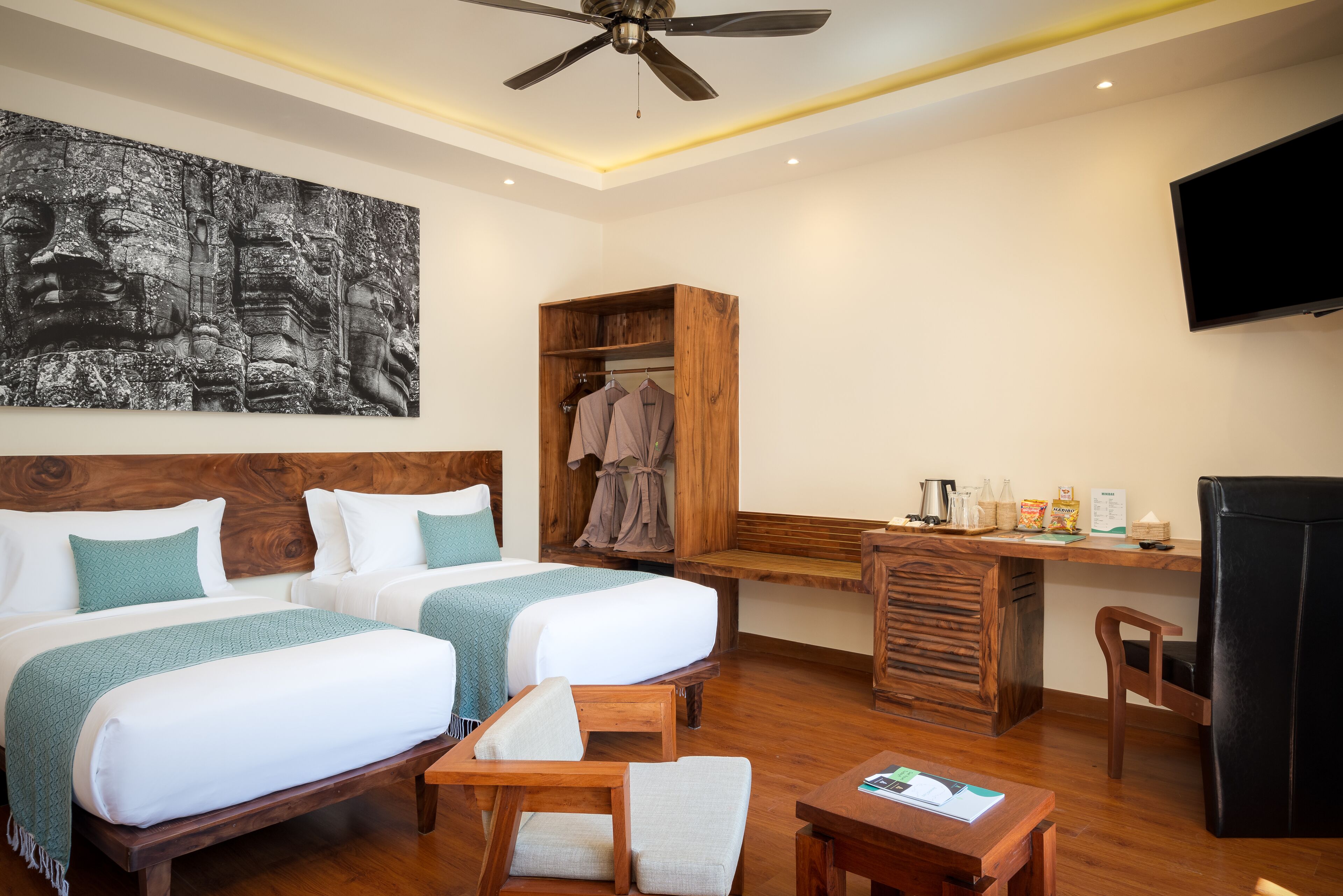A hotel room with two beds, a wooden desk, a television, and a painting on the wall.