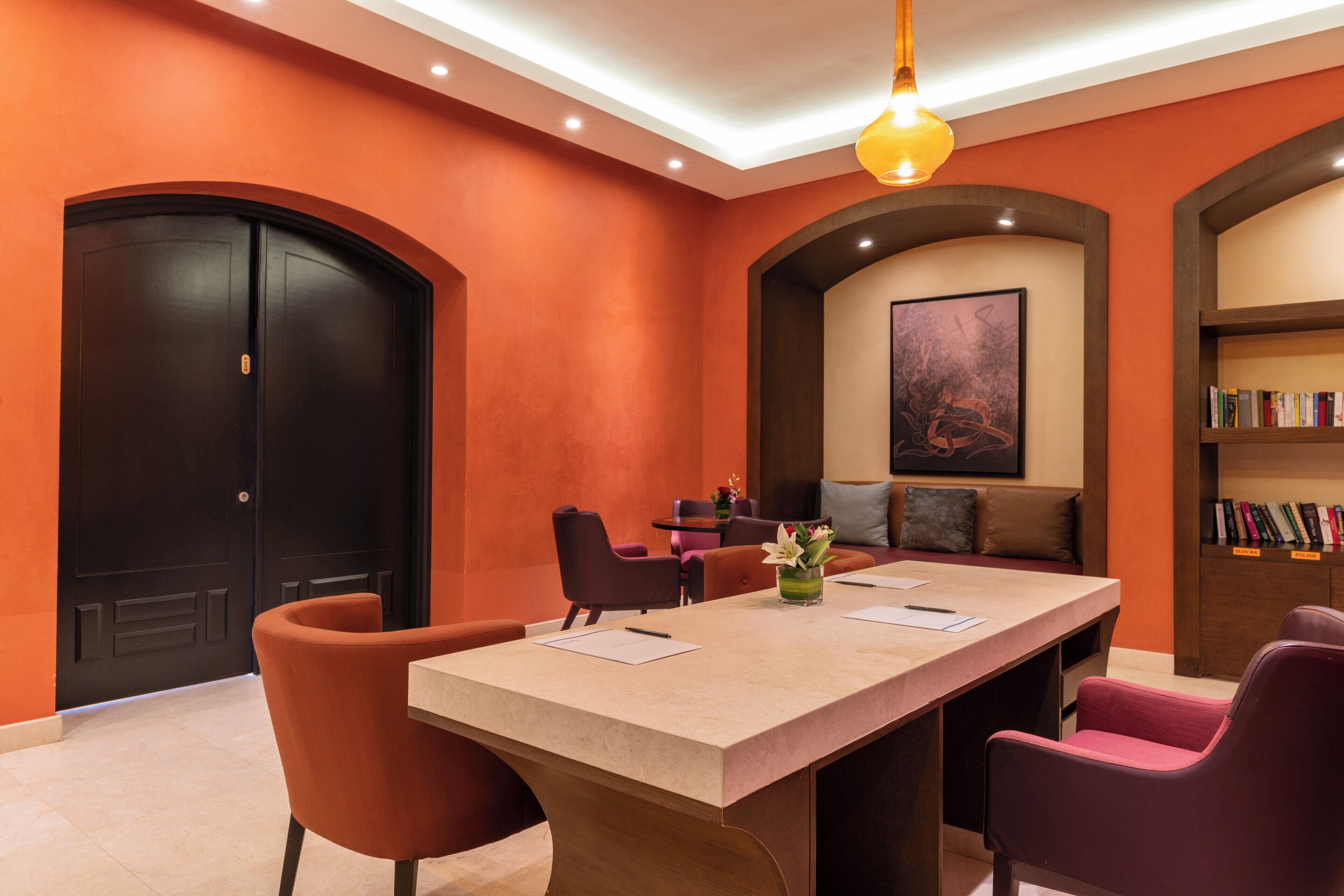 A conference room with a long table, four chairs, a bookshelf, and a painting on the wall.