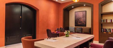 A conference room with a long table, four chairs, a bookshelf, and a painting on the wall.