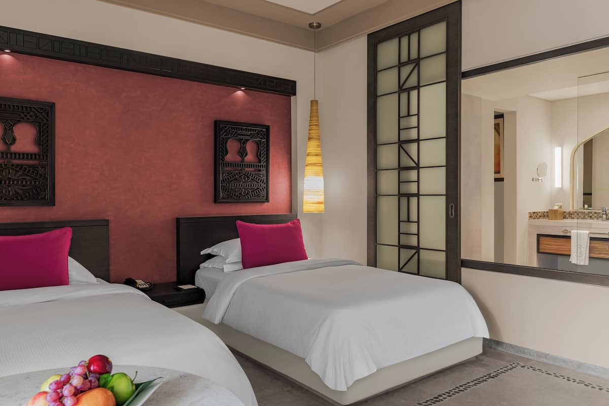 A hotel room with two beds, a large mirror, and a fruit bowl on the nightstand.