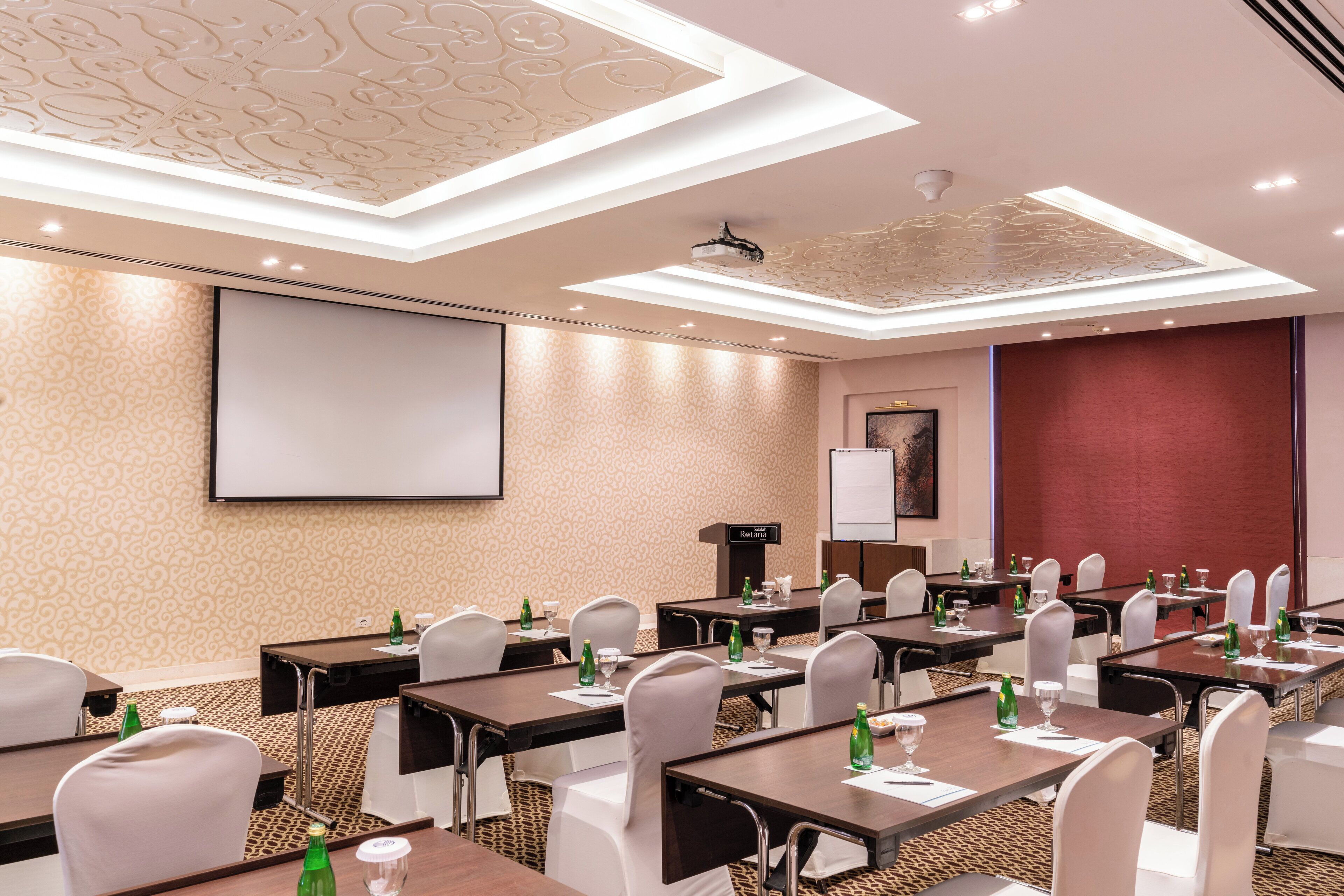 A conference room with tables, chairs, a projector screen, and a whiteboard.