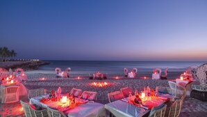 Un área de comedor frente a la playa con mesas dispuestas para dos, cada una con velas y cubertería.