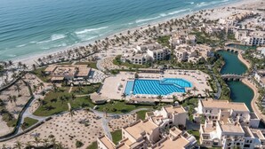 Vista aérea de un complejo turístico con una piscina grande, acceso a la playa y palmeras.