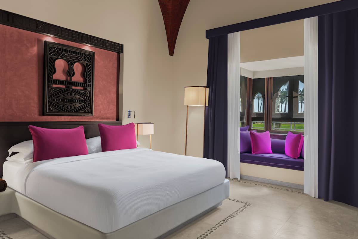 A hotel room with a large bed, a view of a garden through a window, and a decorative wall piece.