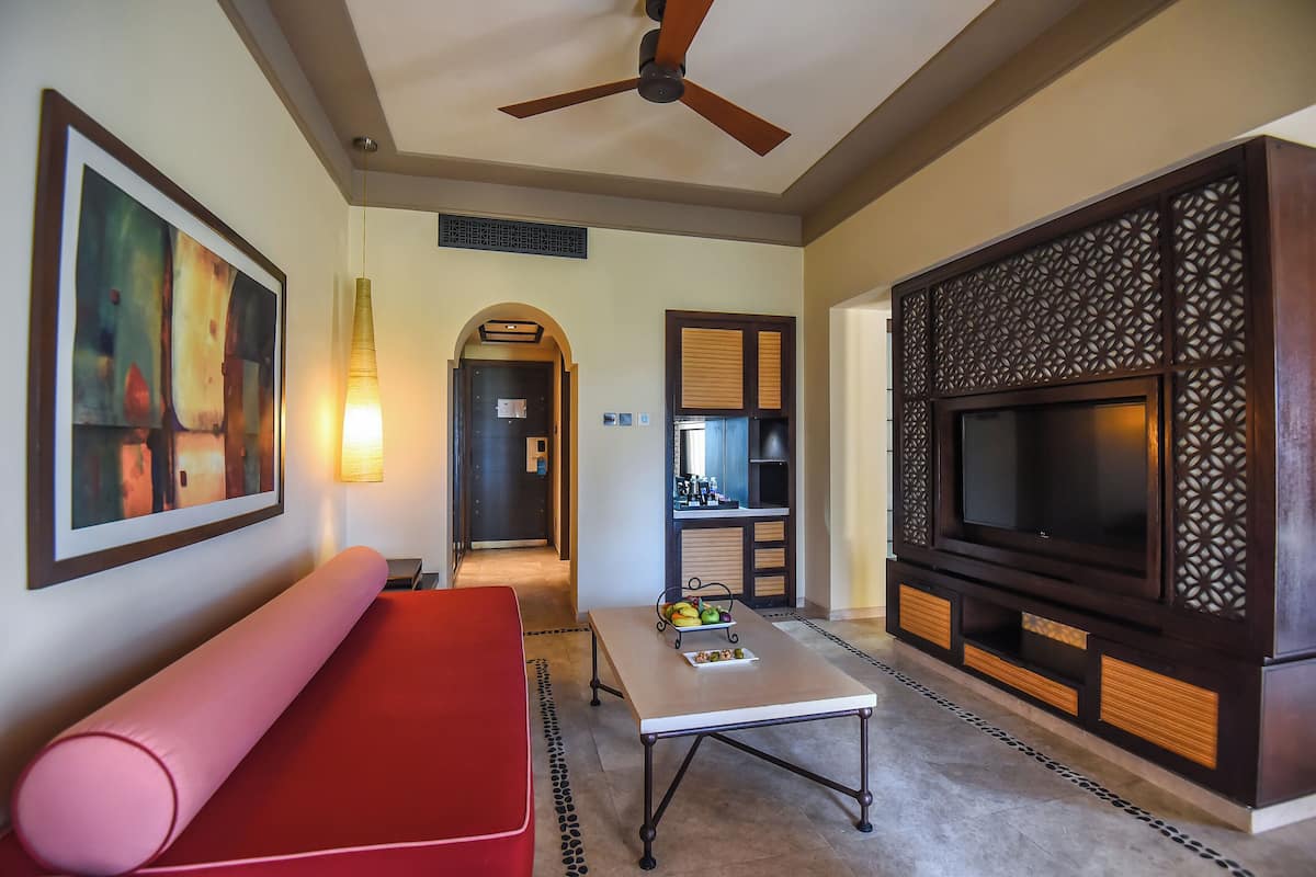 A modern living room with a red sofa, a coffee table with fruit, a TV, and a ceiling fan.