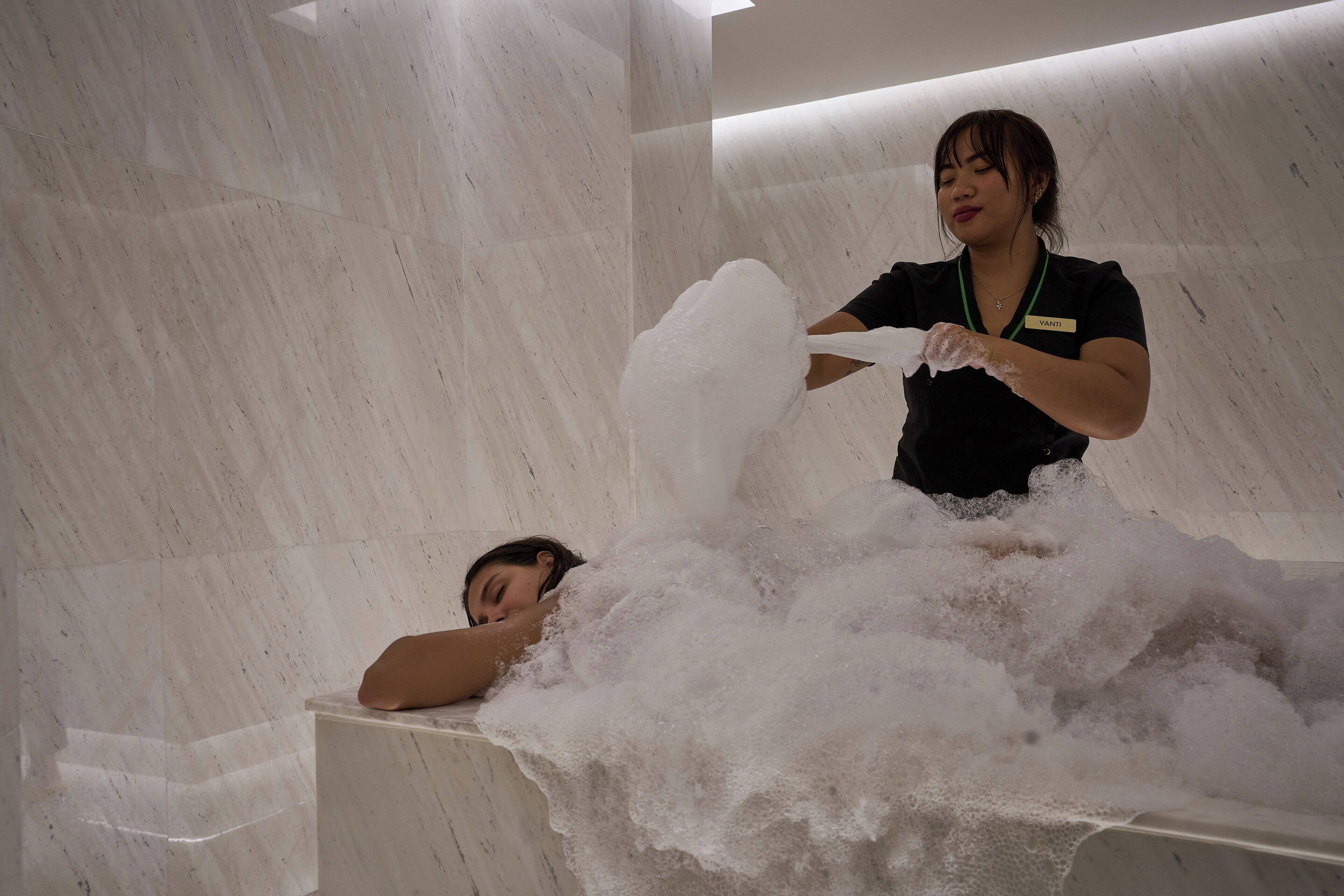 A person in a bathtub filled with bubbles, with a name tag visible.