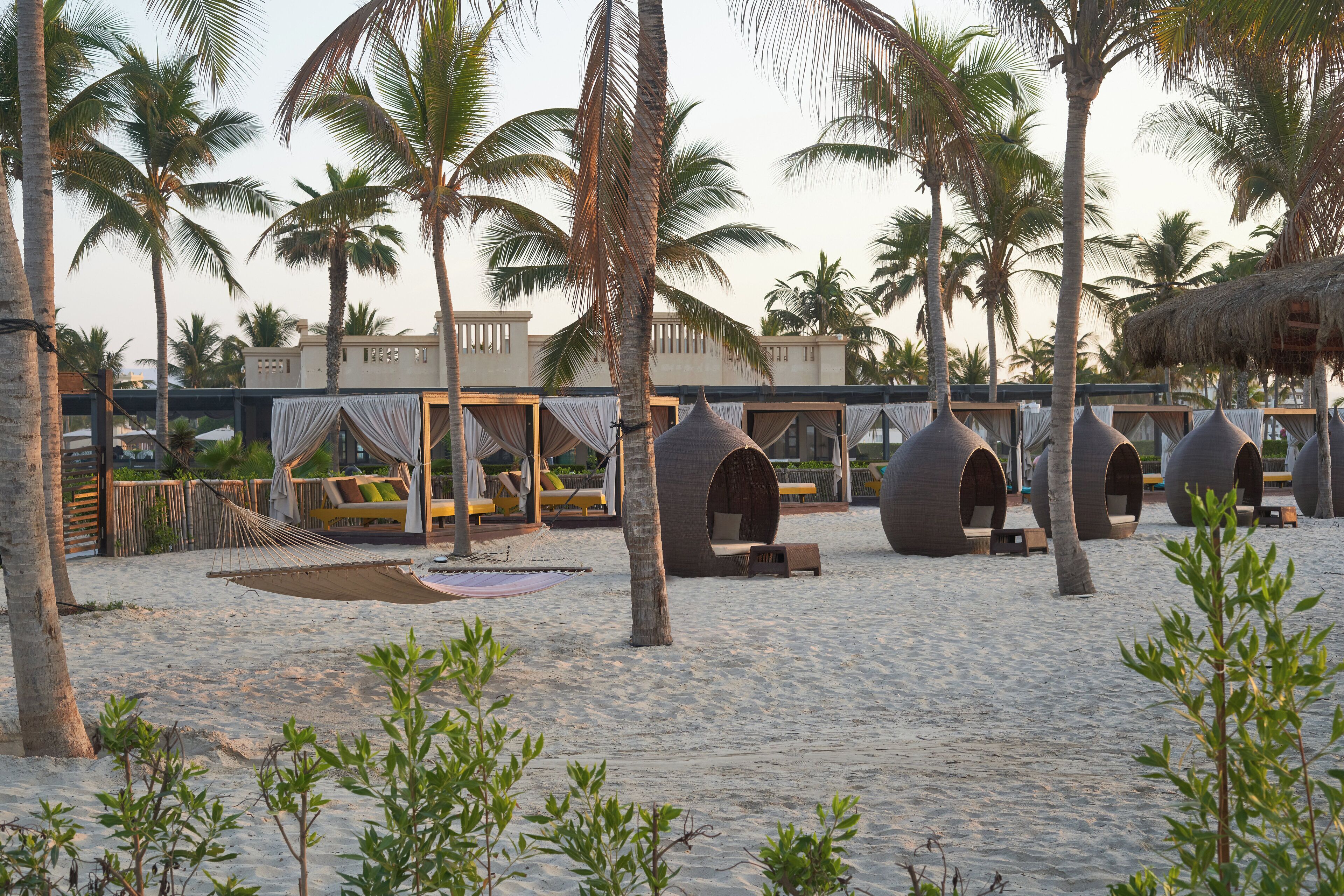 Resort à beira-mar com construções de palha, redes e palmeiras.