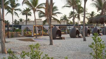 Resort à beira-mar com construções de palha, redes e palmeiras.