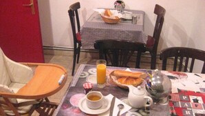 Una mesa para comer con alimentos para el desayuno, una silla y una mesa pequeña con una cesta de pan.