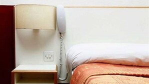 Una habitación de hotel con una cama, una mesita de noche con lámpara y un teléfono.
