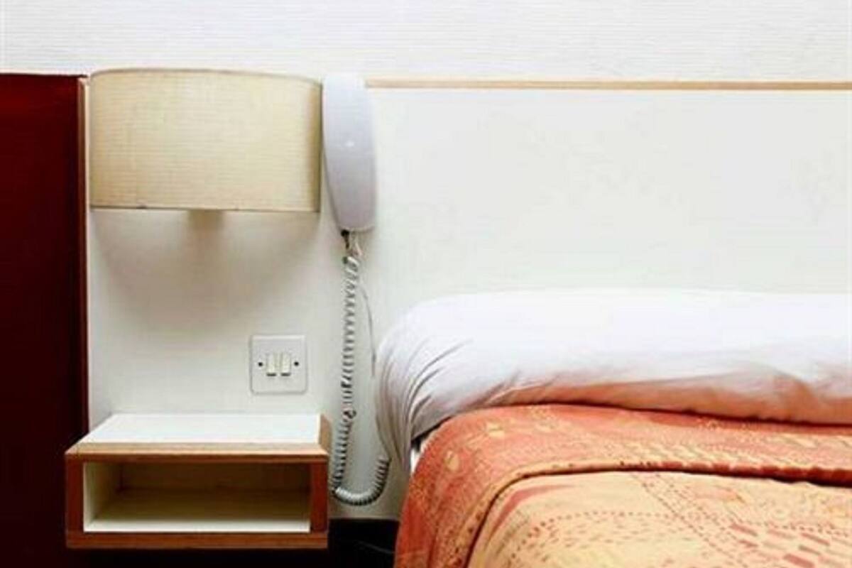 Una habitación de hotel con una cama, una mesita de noche con lámpara y un teléfono.